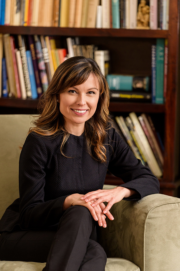 A photo of Professor Basia Ellis sitting in a chair in front of a bookshelf.