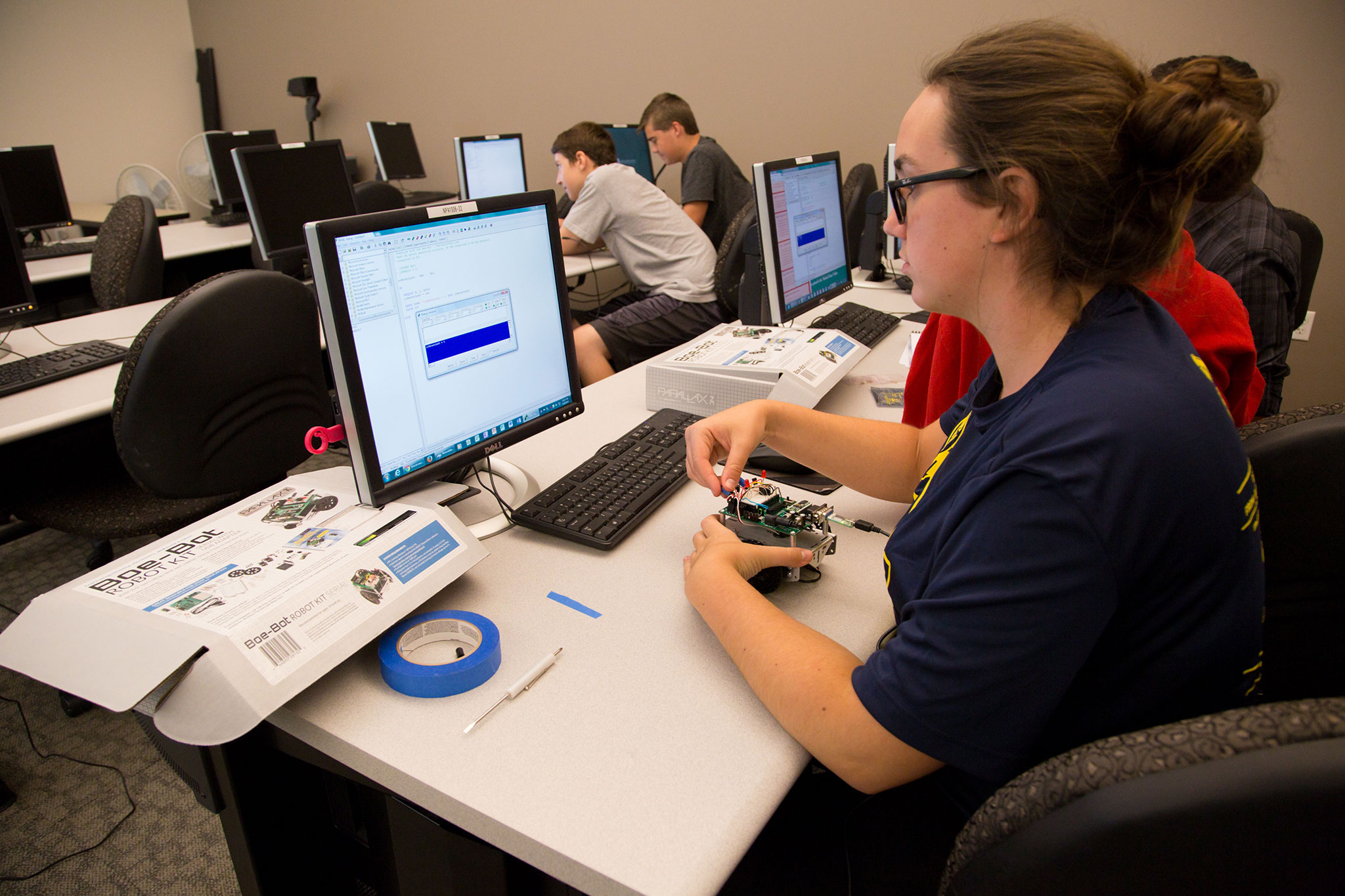 A photo of a high school student sitting a desk programming a robot