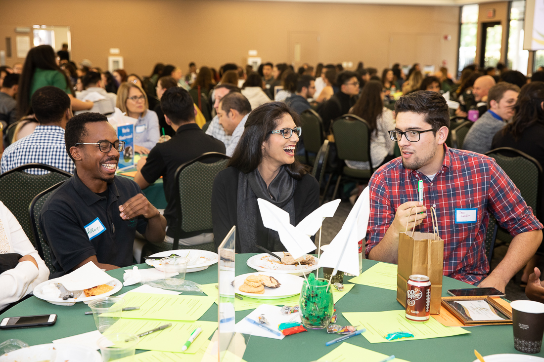 A photo of three students talking and laughing at a circular table.