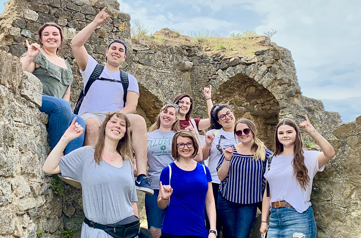 Nine students in an outdoor location in France, making the Stingers Up signal with their hands