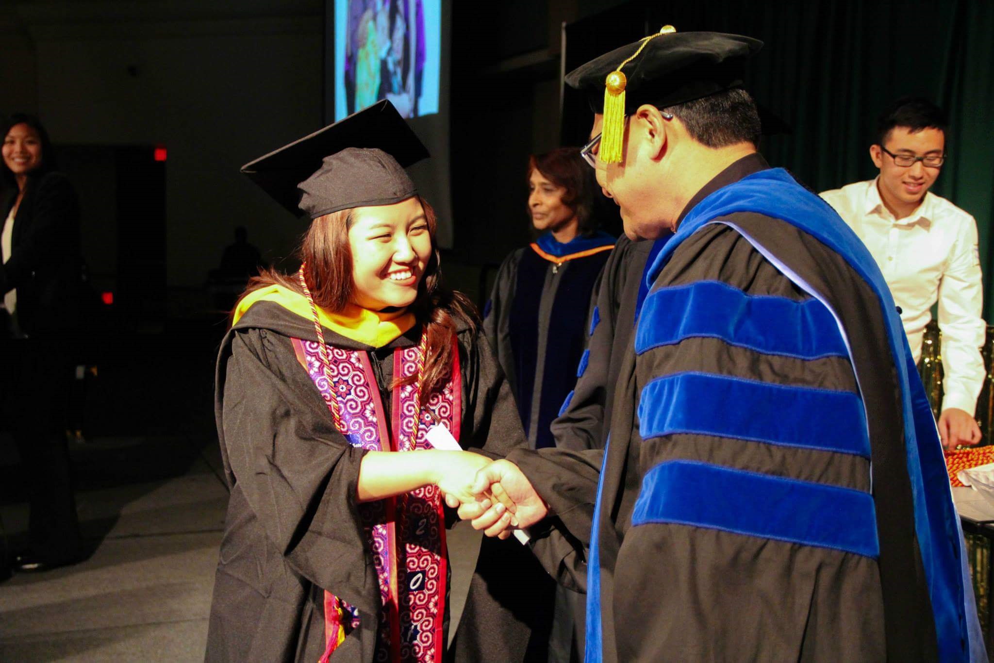 A photo of a Hmong student in graduation regalia receiving her degree