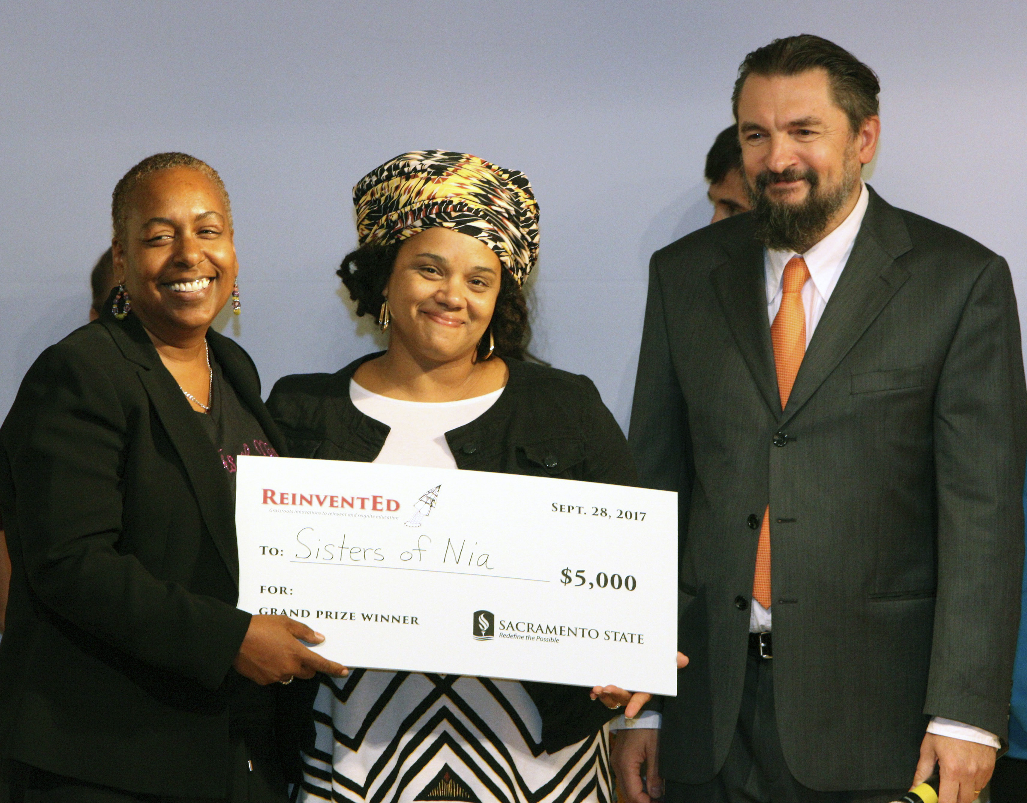 Sisters of Nia co-founders Synthia Smith and Malika Hollinside, holding a $5,000 prize check alongside College of Education Dean Sasha Sidorkin.