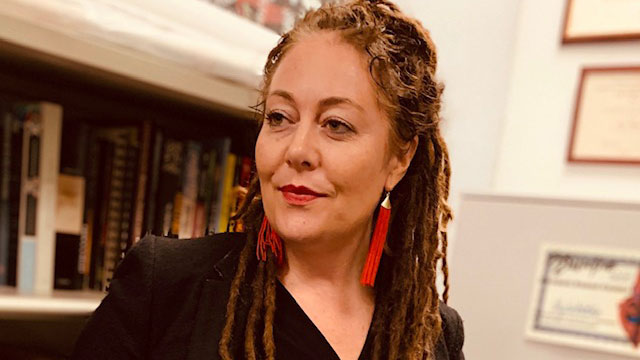 Vajra Watson looking to the left, standing in front of a bookshelf