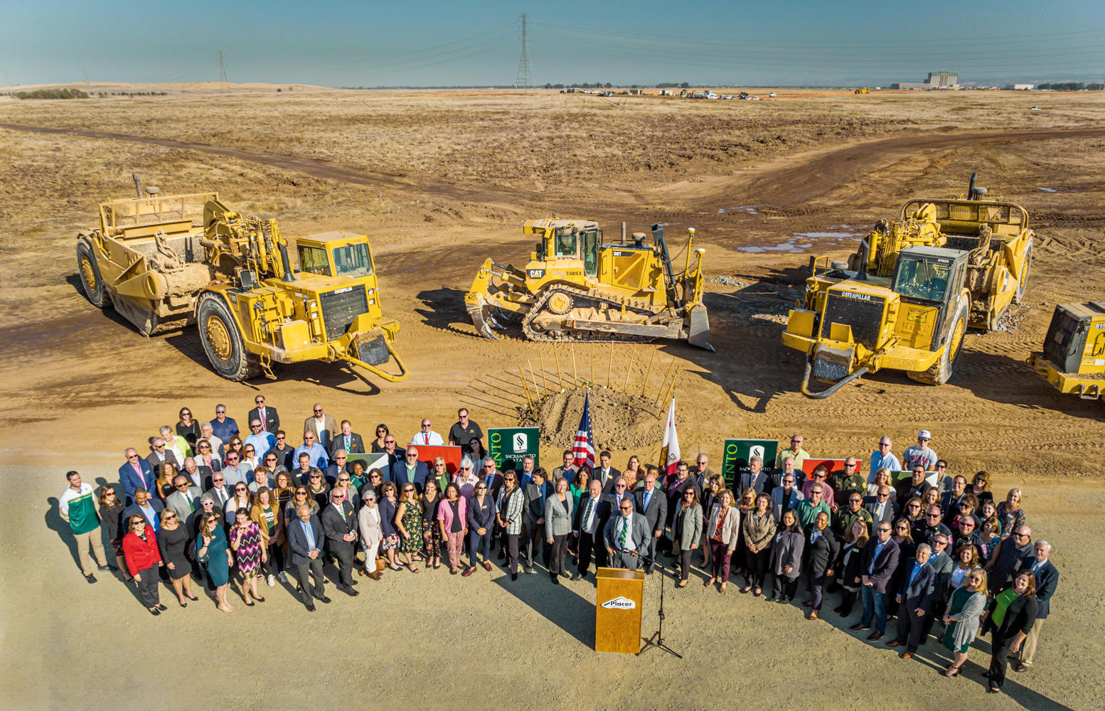 An overhead drone group shot image of the attendees of a recent Placer One groundbreaking ceremony along with a line of construction vehicles behind them.