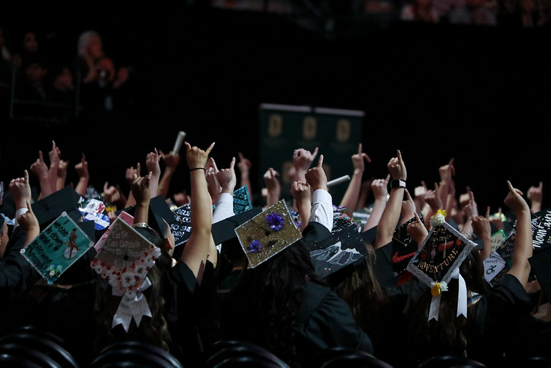 commencement graduates with caps on and stingers up fingers up