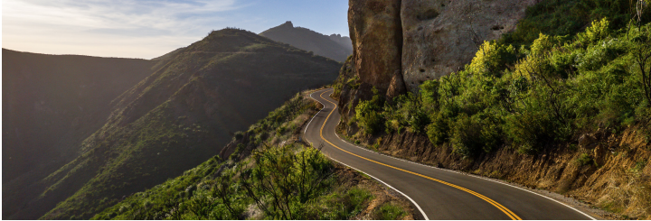 A winding 2-lane road in forested mountains.