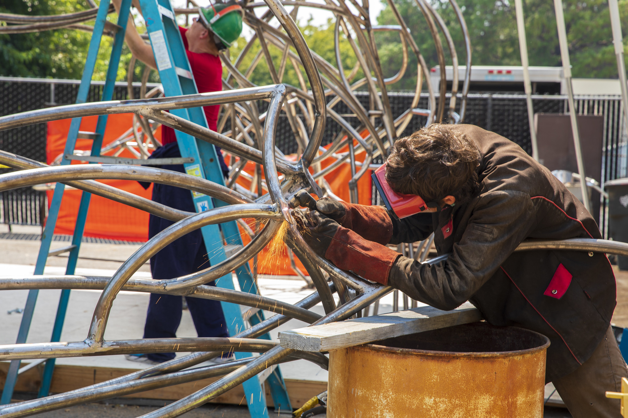 A student wearing safety equipment uses power tools on a metal sculpture