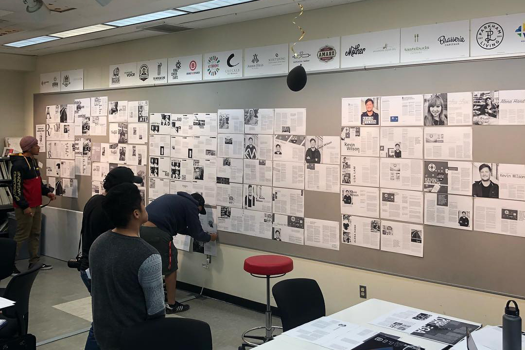 Students view their printed layouts on a critique board while working on a magazine together