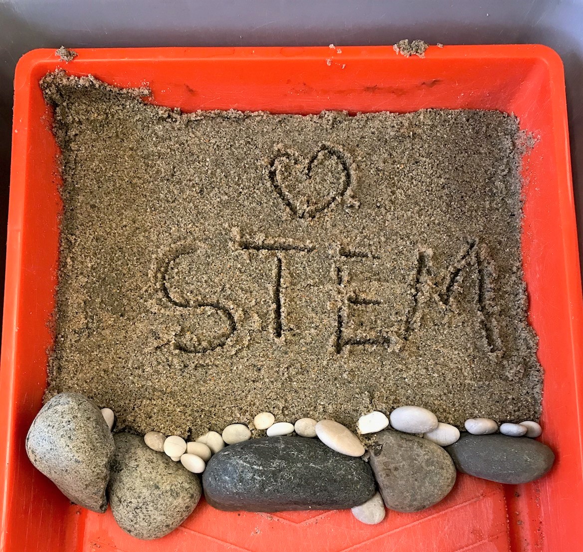 Photo of bucket with sand into which [heart] STEM has been inscribed