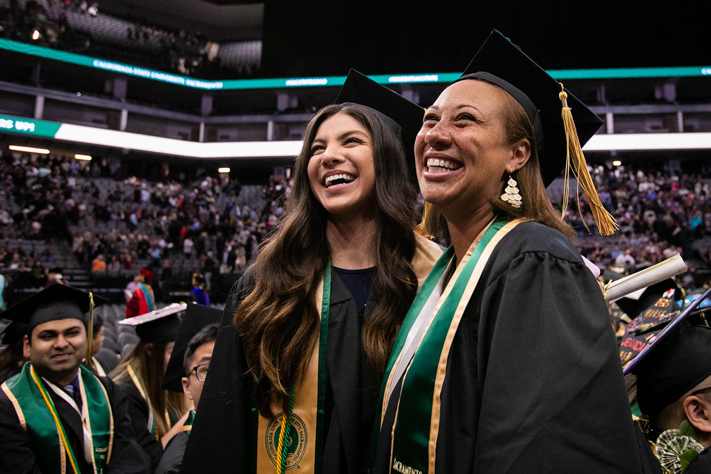 Two female graduates smile from the floor of their commencement ceremony