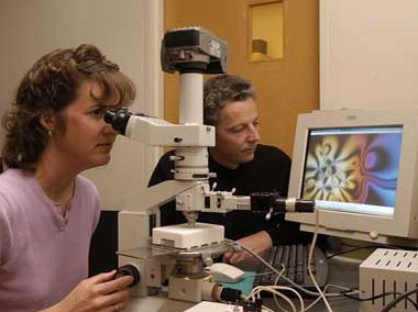 Student looking at liquid crystals through microscope with professor