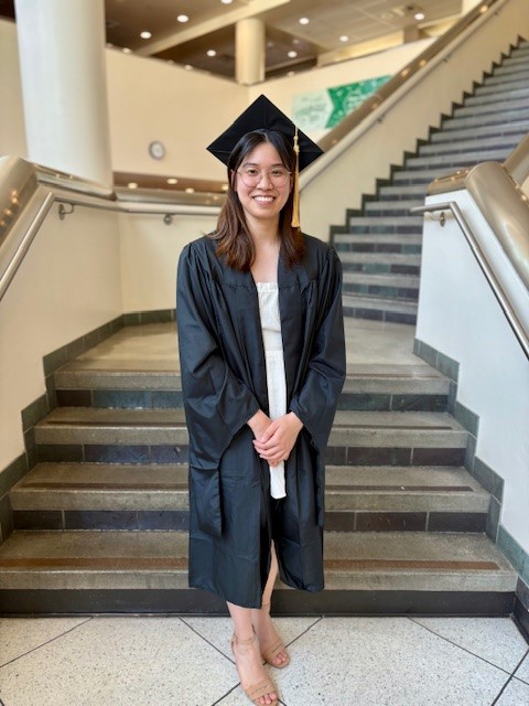 Woman in cap and gown smiling and posed in front of stairs