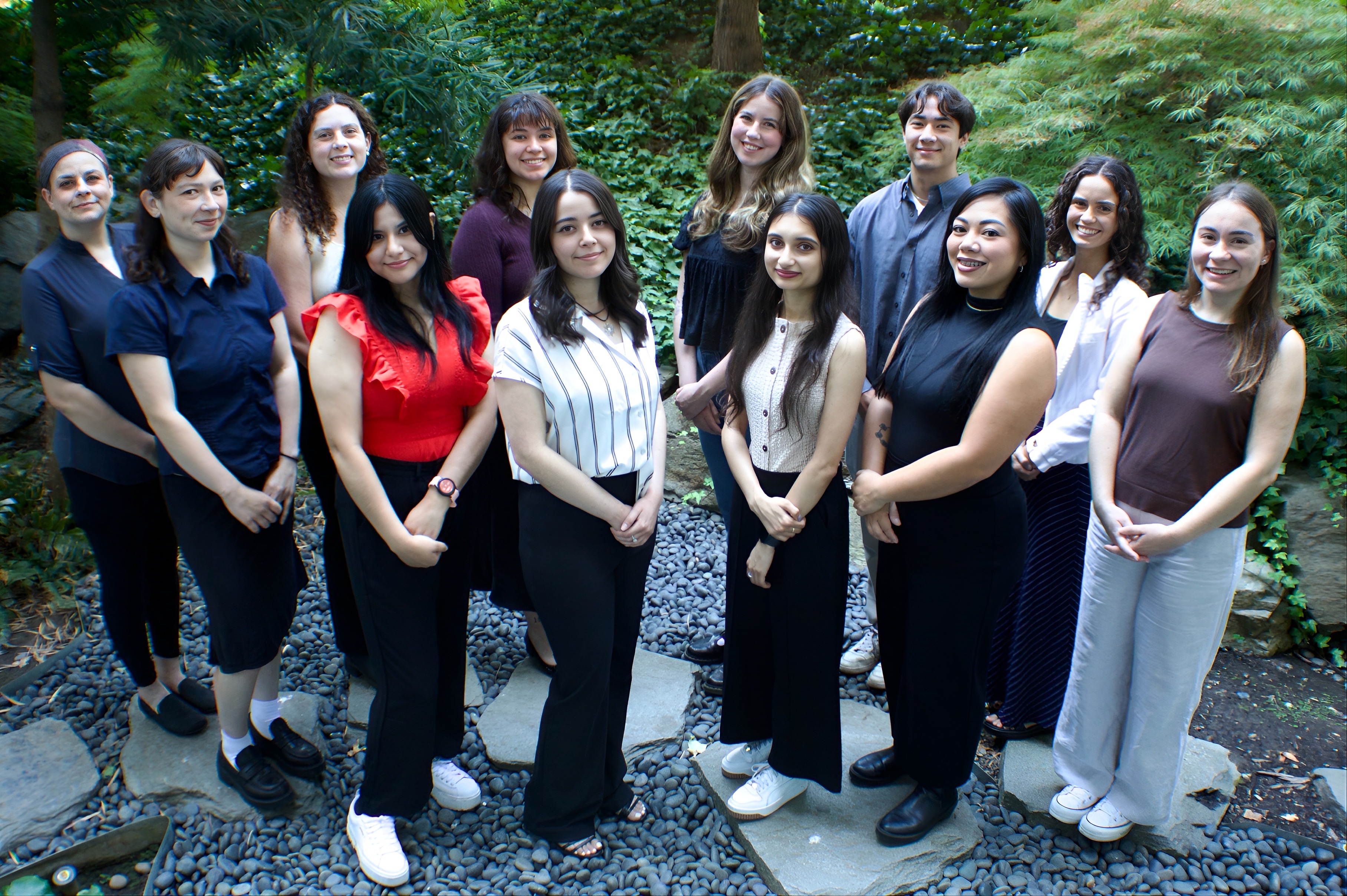 10 people in photo arranged in a front facing V shape with greeny background standing on pebbles and rocks