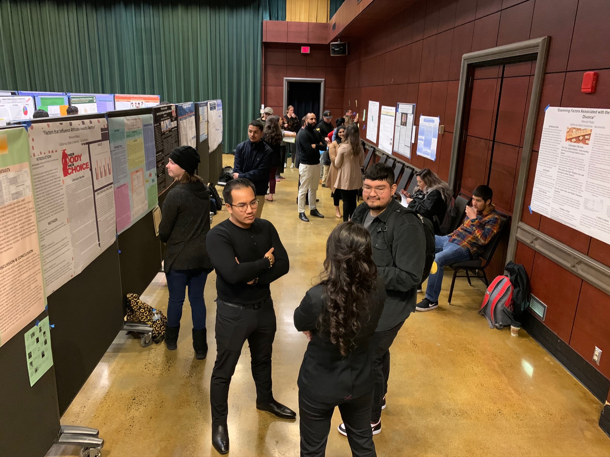 A group of 8 students talking among themselves, in front of their presentations.