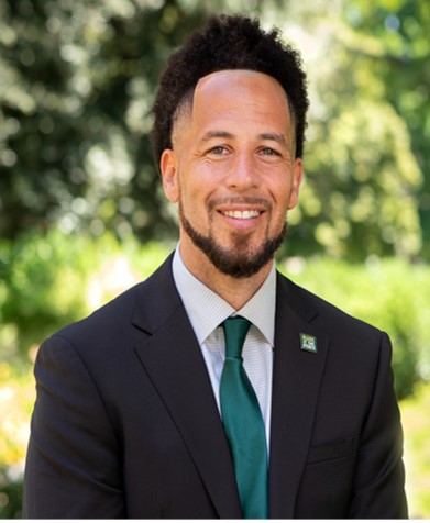 Headshot photo of Sac State President J. Luke Wood in a dark suite with light shirt and green tie. 