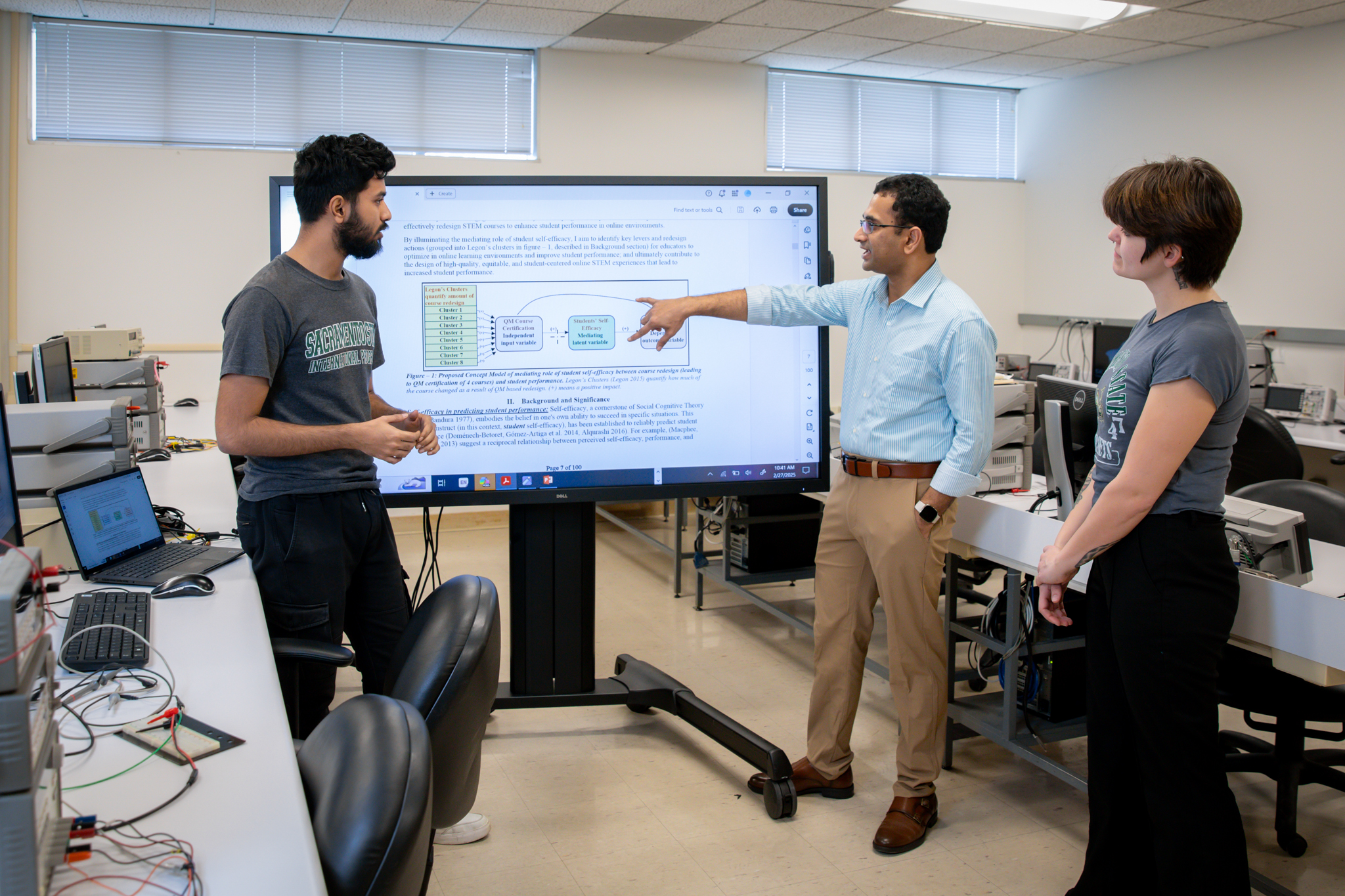 Praveen Meduri points to a display screen as two other students look.