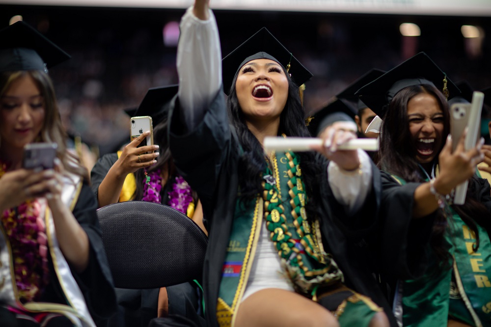 Two female presenting students celebrate in cap and gown at commencement