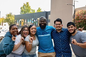 Six students arm in arm with the Sacramento mural in the background