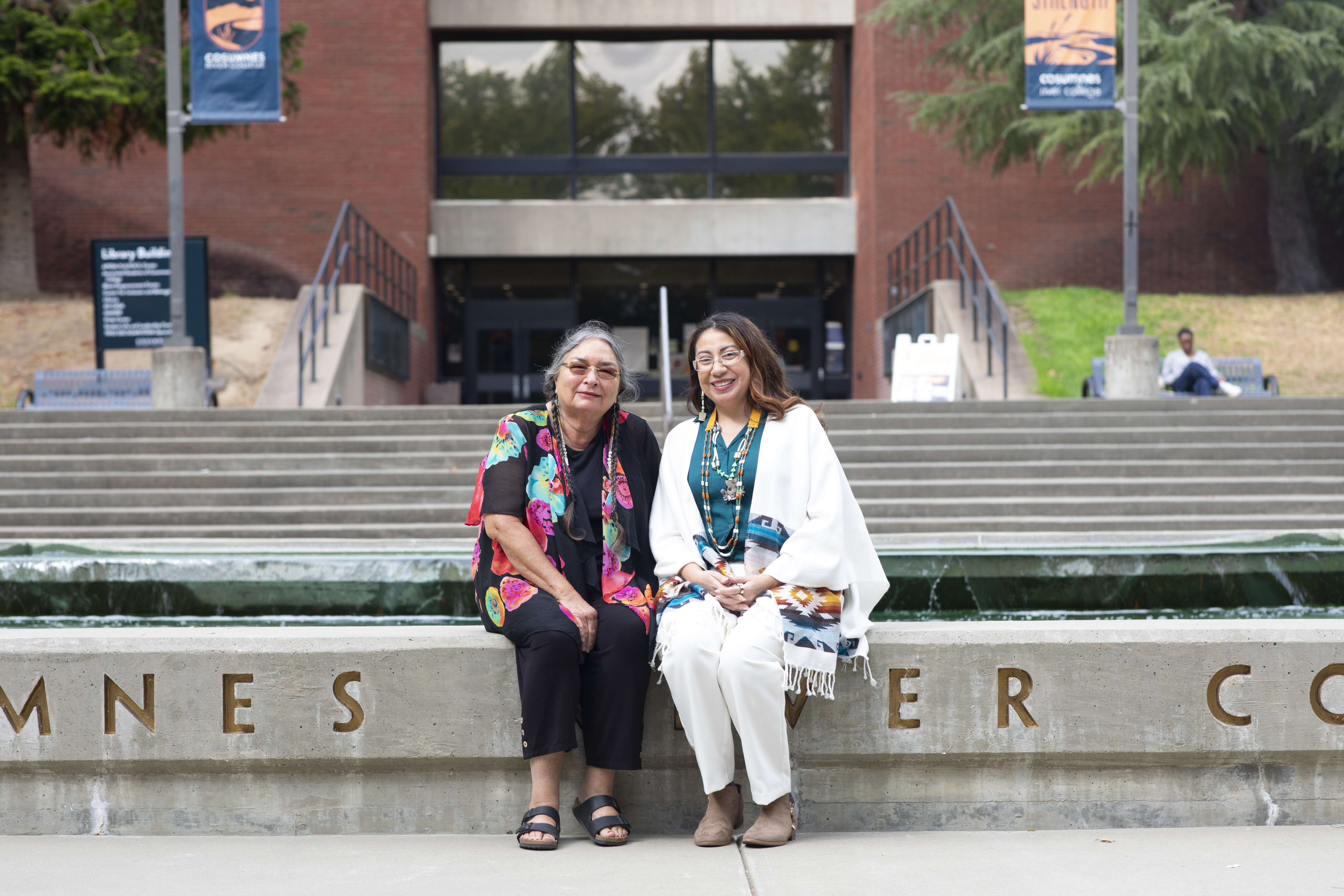 Anne Descalzo and Rachel Zillner sitting in front of a colorful wall reading "Belong Here."