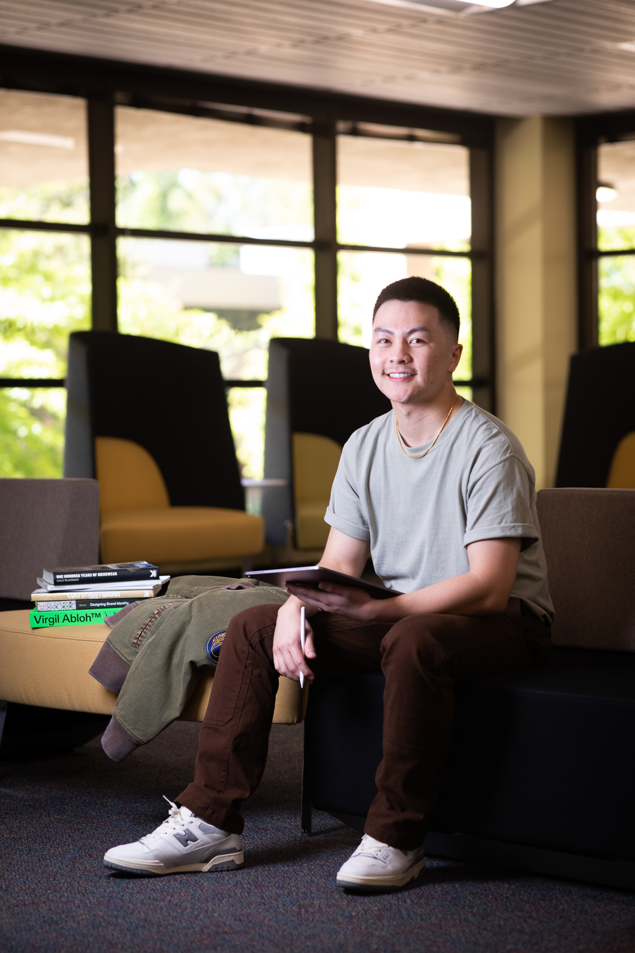 Jason Vu, creator of men's clothing line AUTHMADE, smiles while sitting with his iPad in one hand and electronic pencil in the other hand, tools he uses to design his clothing.