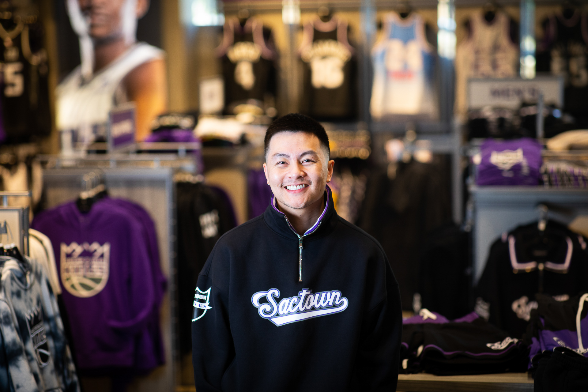 Jason Vu, founder and creative director of AUTHMADE, a men’s clothing line that specializes in apparel for the Sacramento Kings and other NBA teams, poses in the Kings Team Store wearing one of his sweatshirts that reads "Sactown" in stylized blue font.