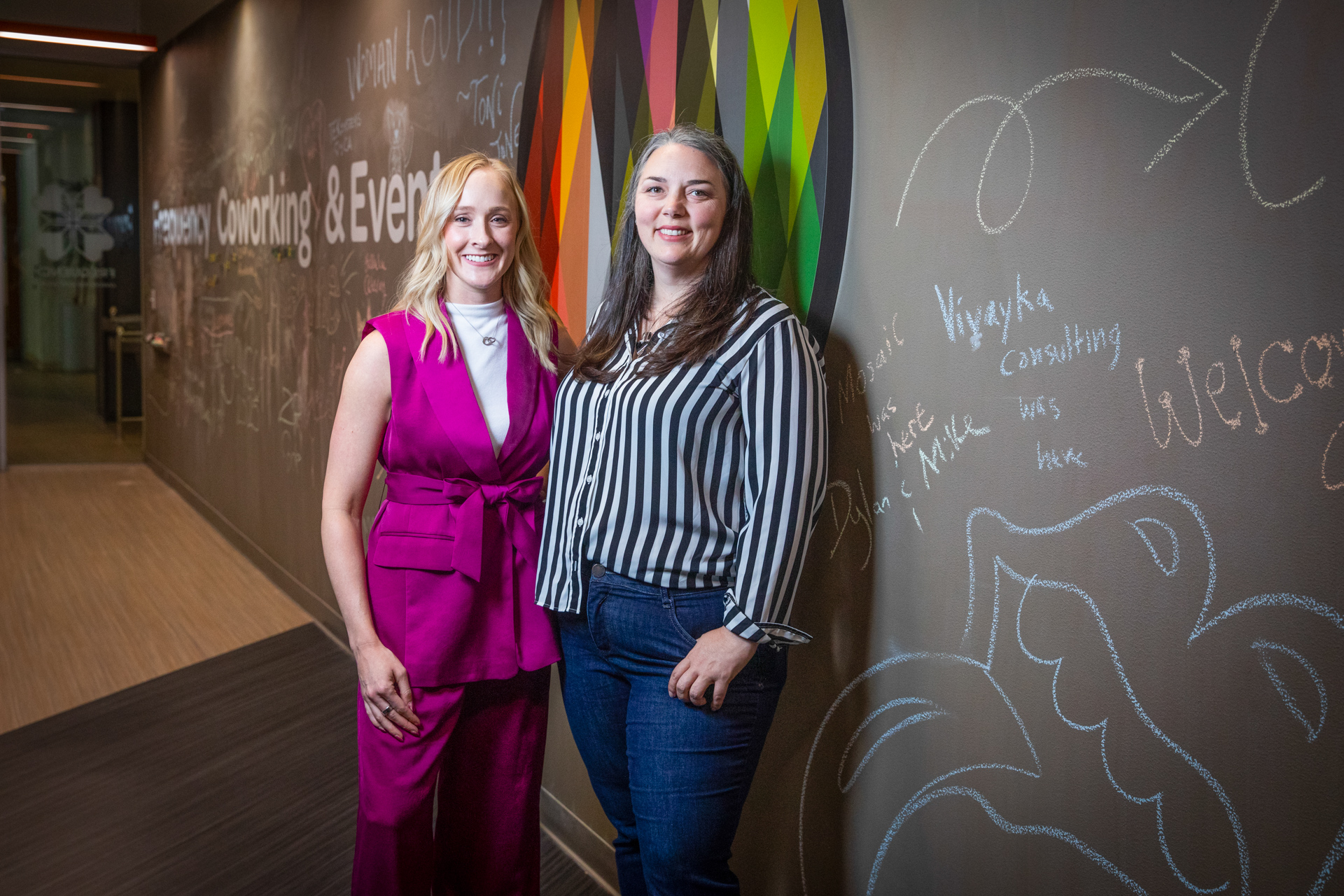 Anne Descalzo and Rachel Zillner standing in front of a long wall decorated with chalk drawings.