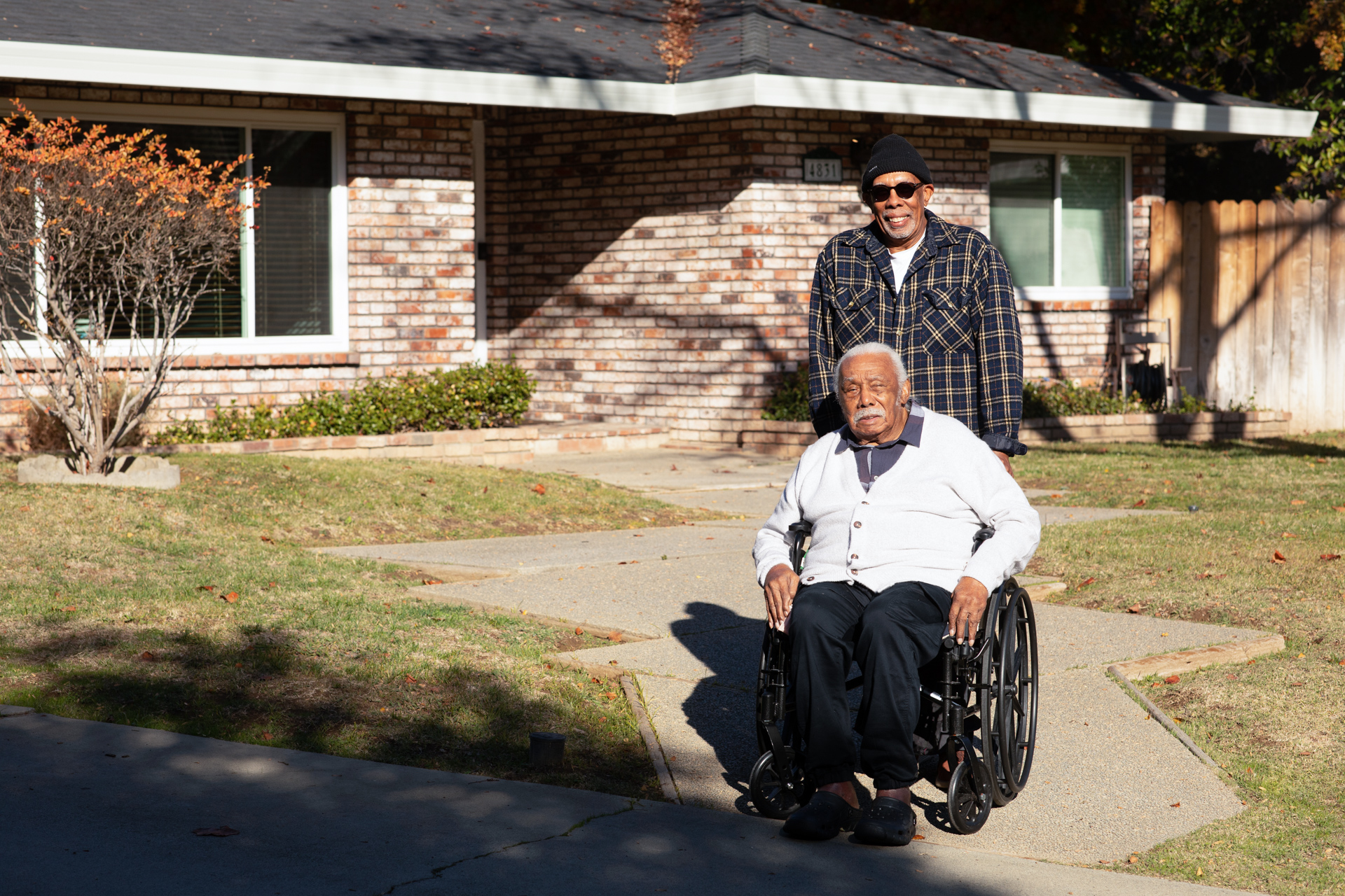 Anthony Francis in a wheelchair with his son pushing him along the front sidewalk of their home. 