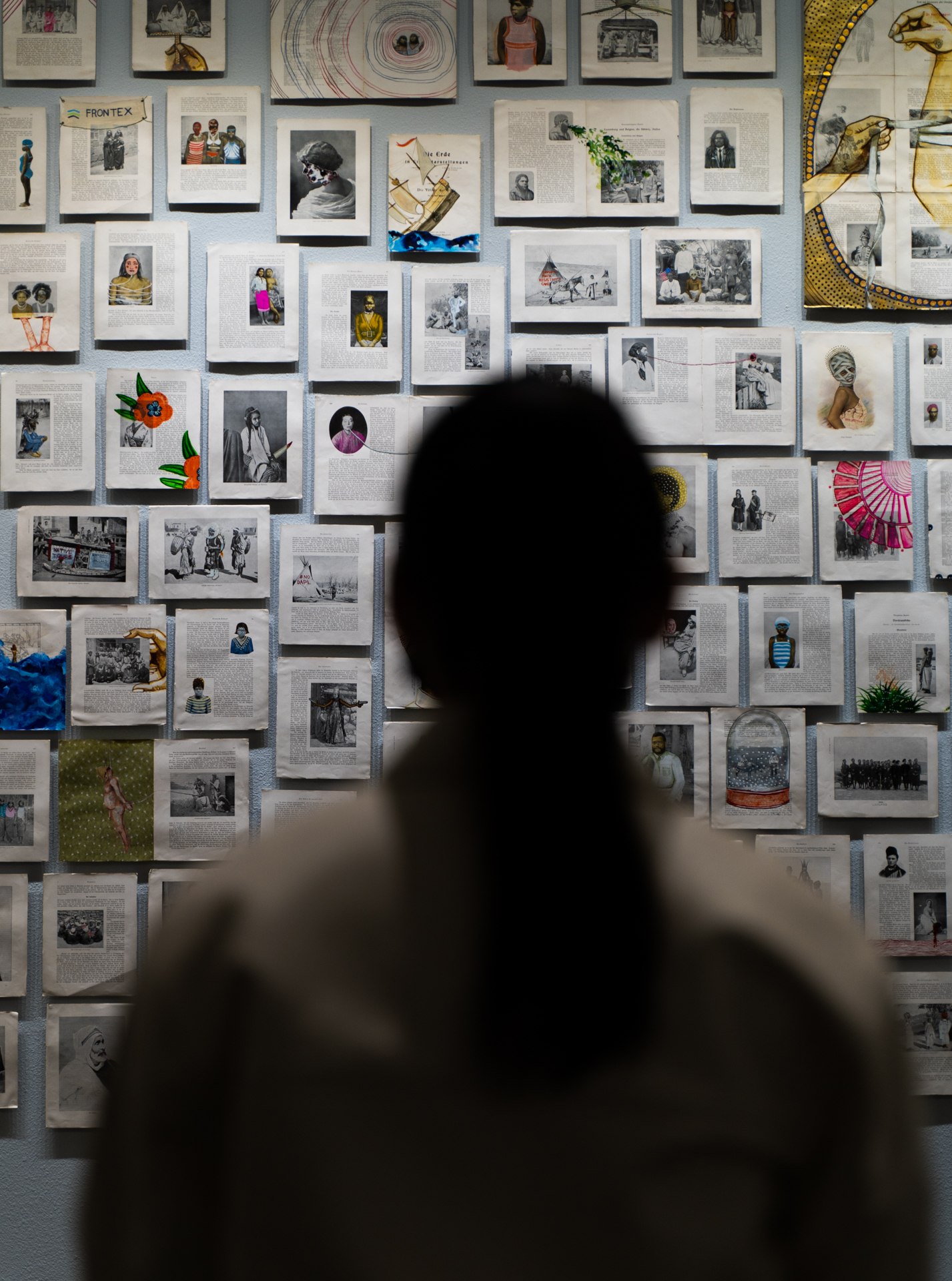 A person viewing a wall full of small paintings