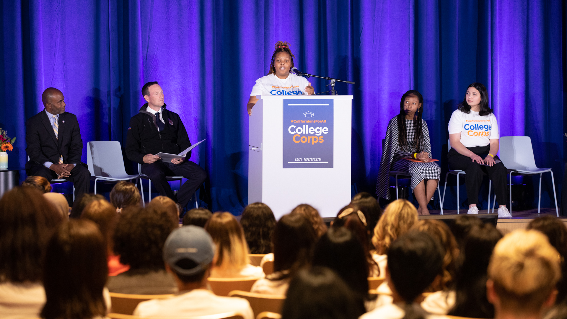 Sac State student Tia Rowe speaks at a podium on stage during an event for the inaugural #CaliforniansForAll College Corps class.