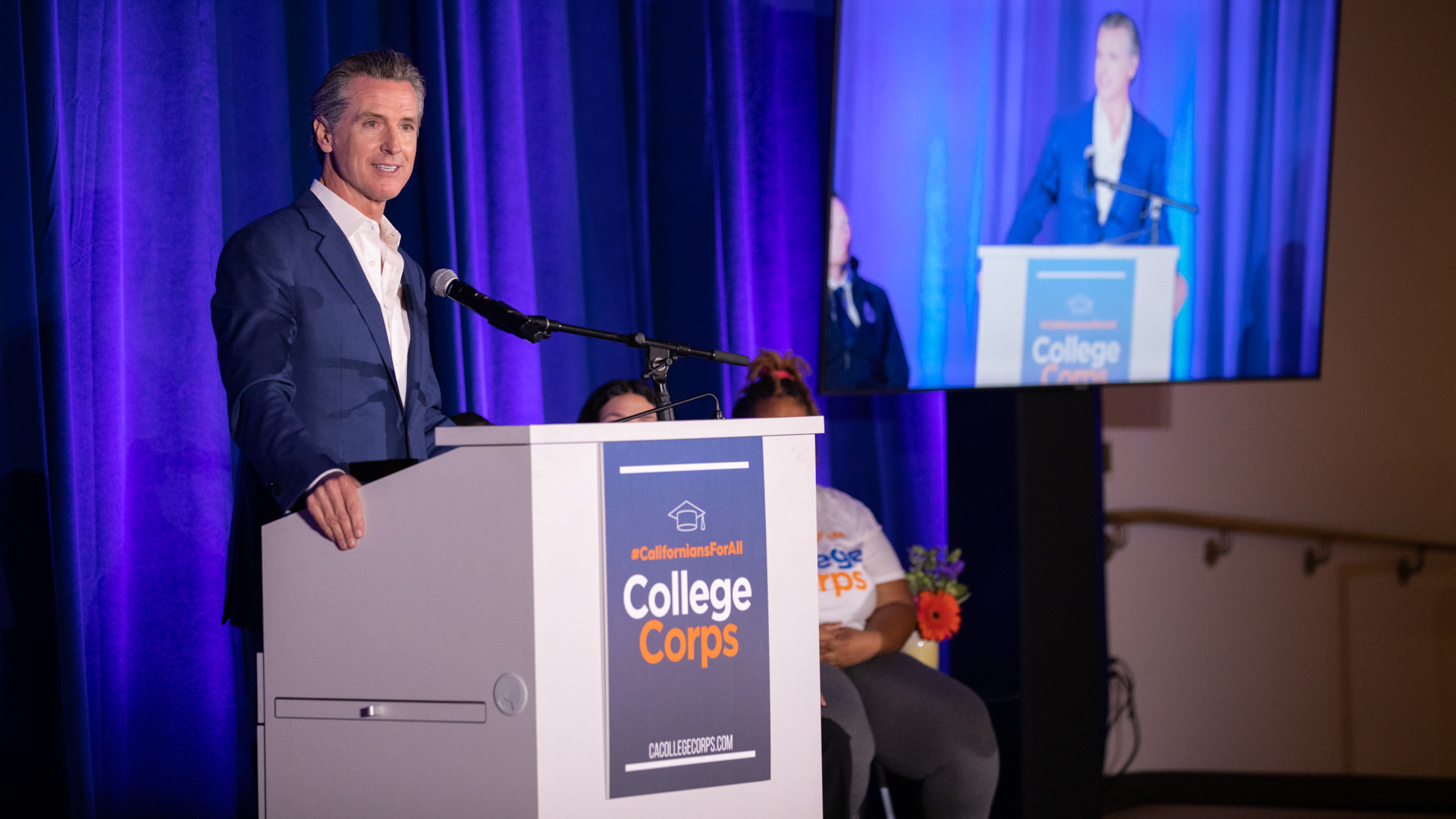 California Gov. Gavin Newsom speaks at a podium on stage during an event for the inaugural #CaliforniansForAll College Corps class.