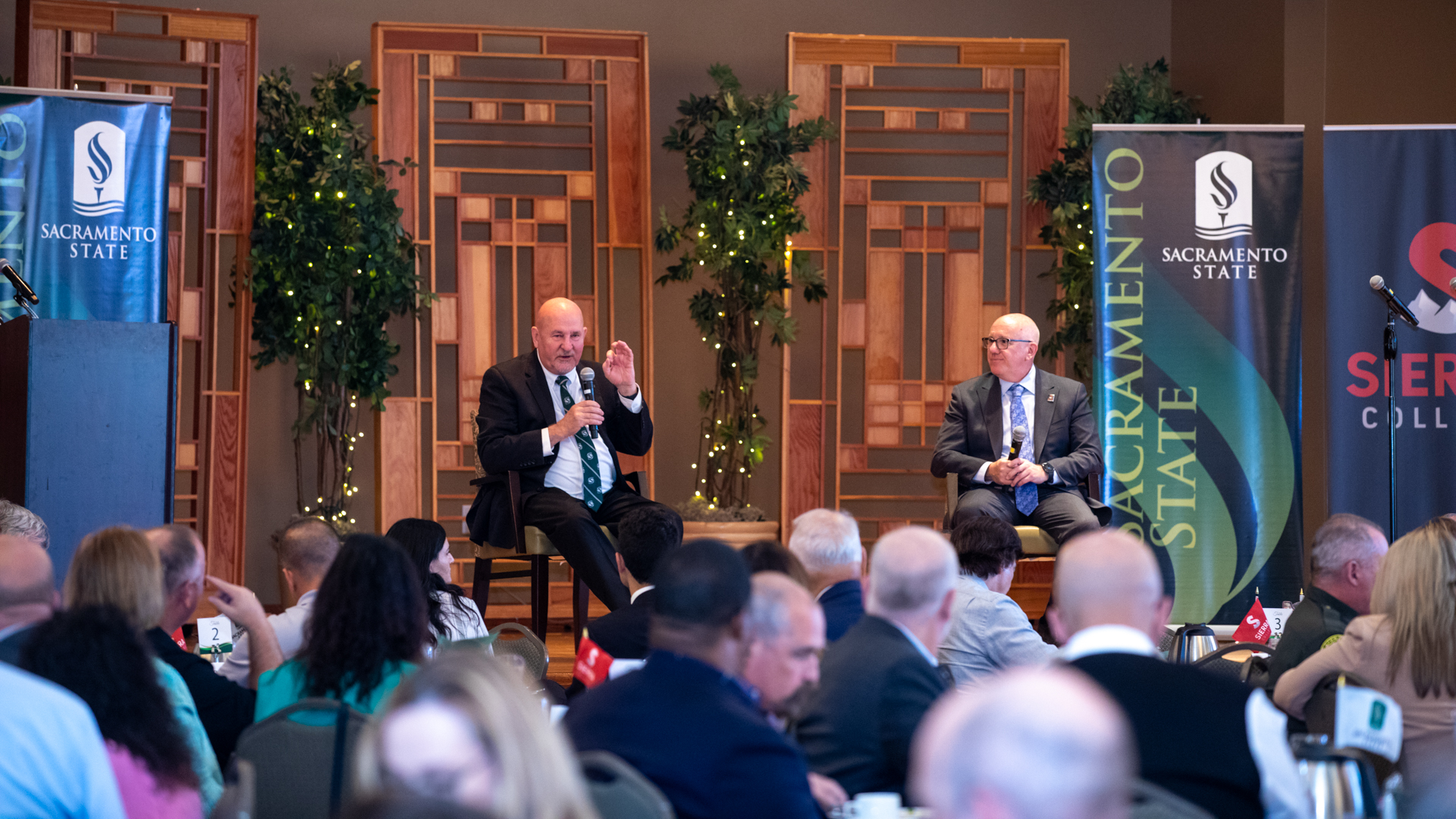 Sac State President Robert S. Nelsen and Sierra College President Willy Duncan speak on stage next to banners during a luncheon at the Placer One groundbreaking event.