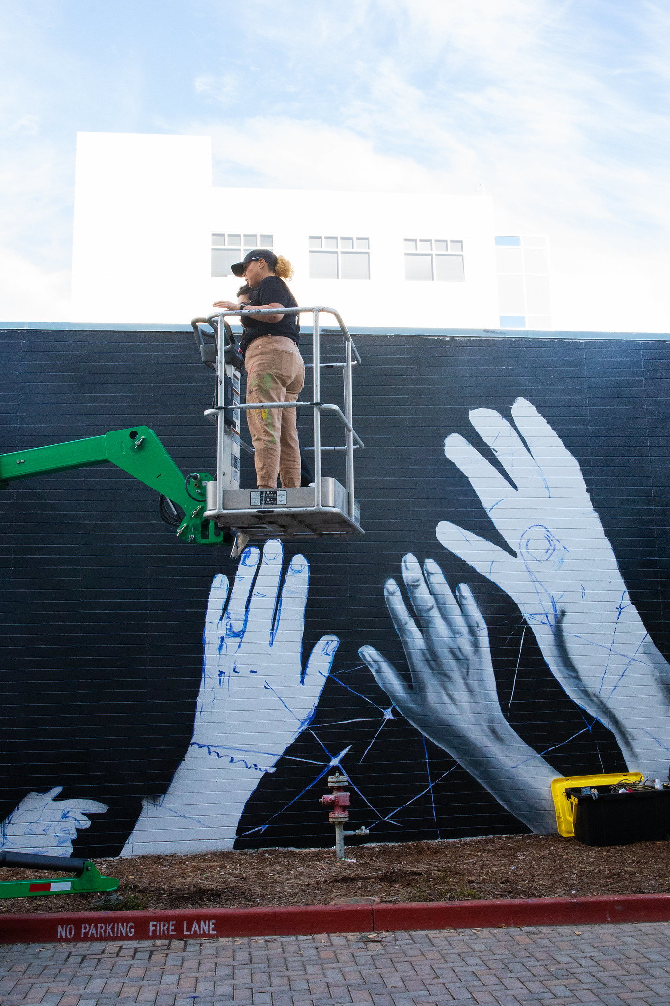 A woman, on a lift, above a mural depicting white hands on a black background