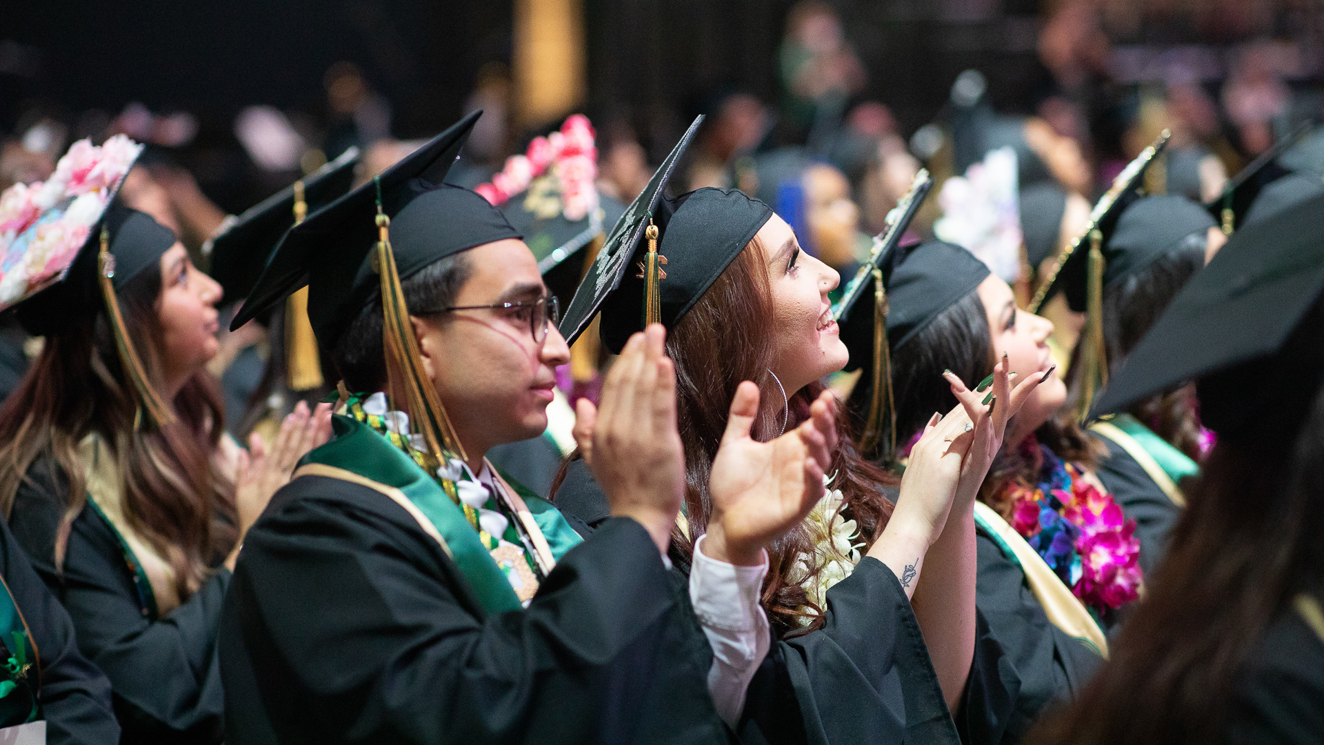 Graduates wearing caps and gowns and other garb cheer during Sac State Commencement. 