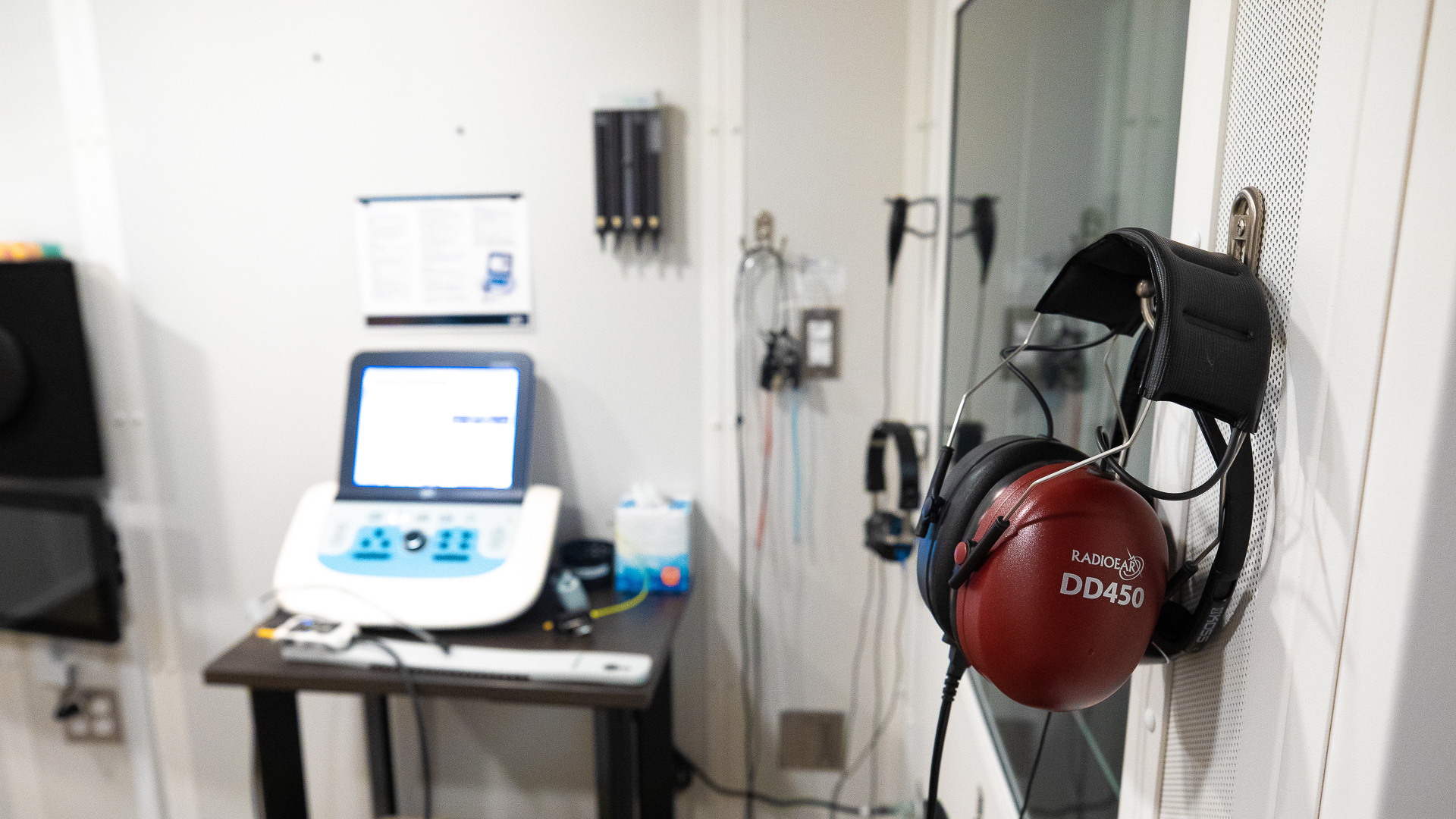 A hearing exam room, with a large set of red headphones on the wall and computer in the background