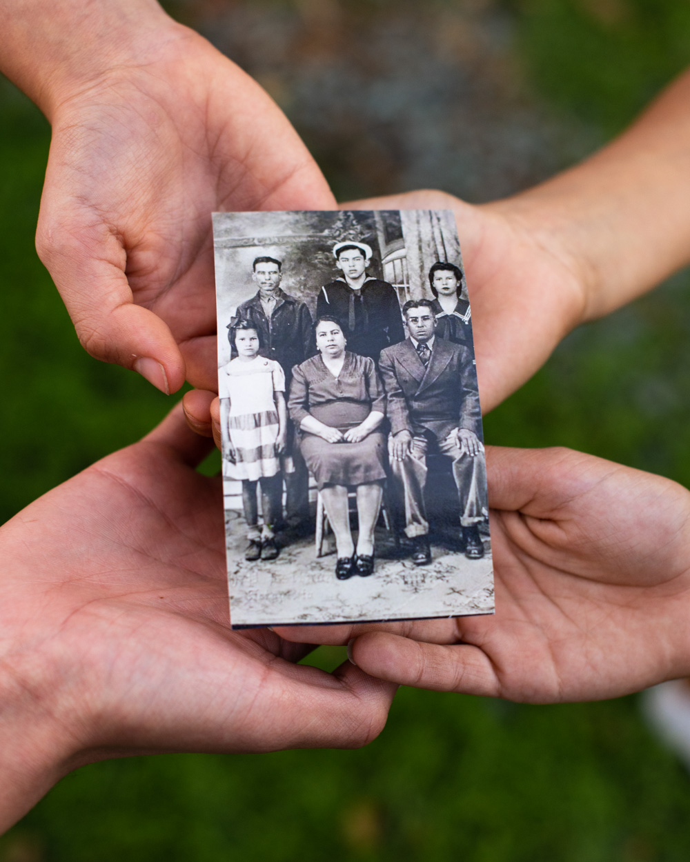 Four hands holding a black and white photo of five people
