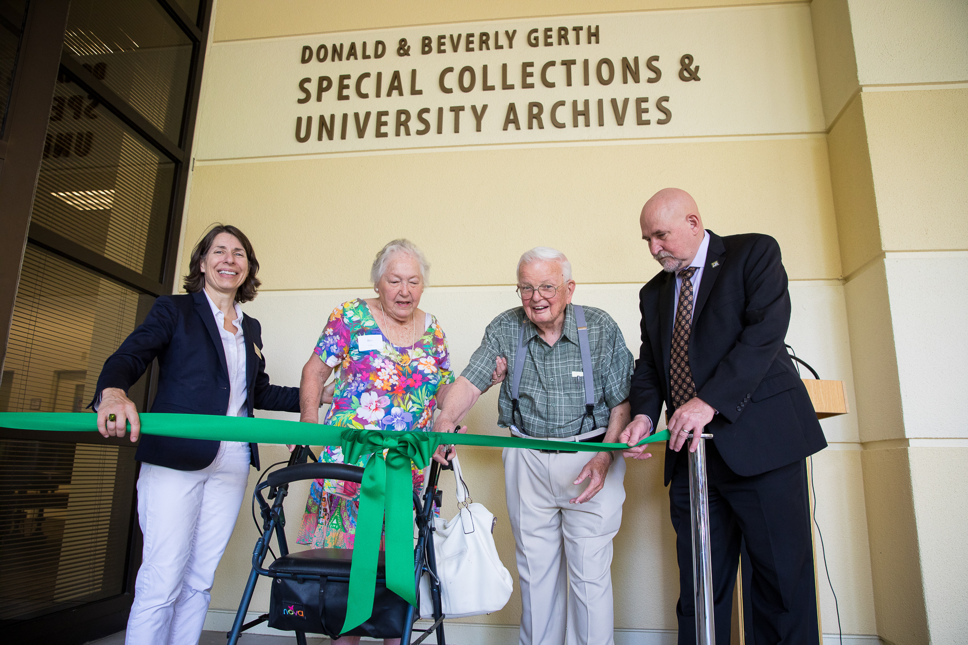 University Librarian Amy Kautzman, Beverly Gerth, Donald R. Gerth, and Sac State President Robert Nelsen, standing as Donald Gerth cuts a green ribbon, in front of the University's Special Collections and Archives