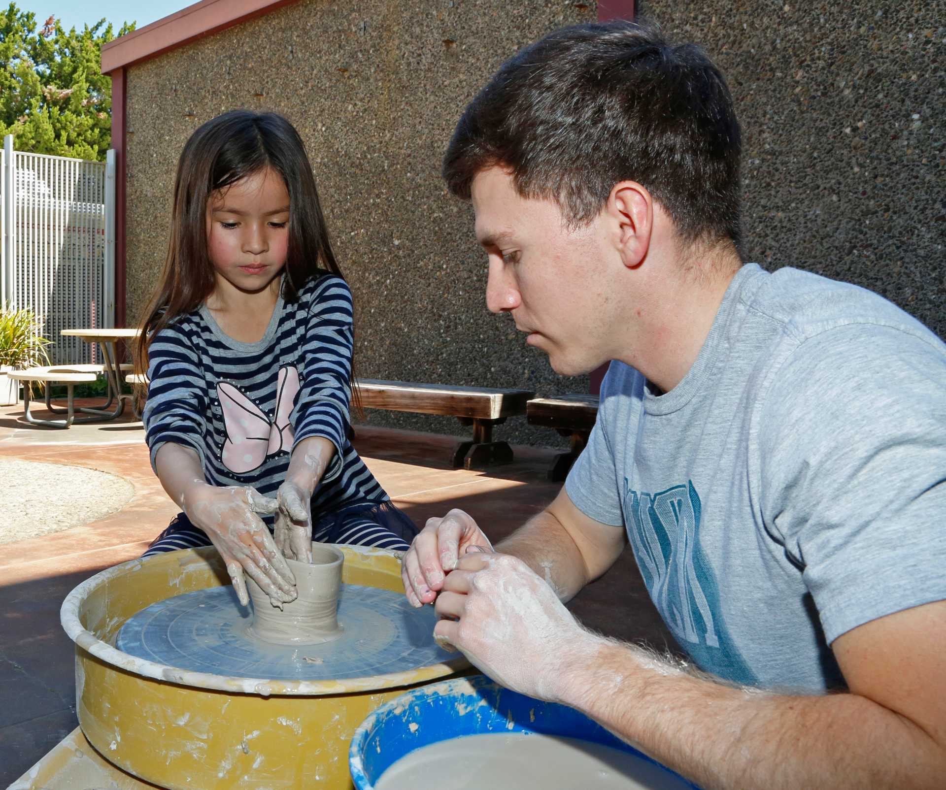 A girl shapes pottery while a man looks on