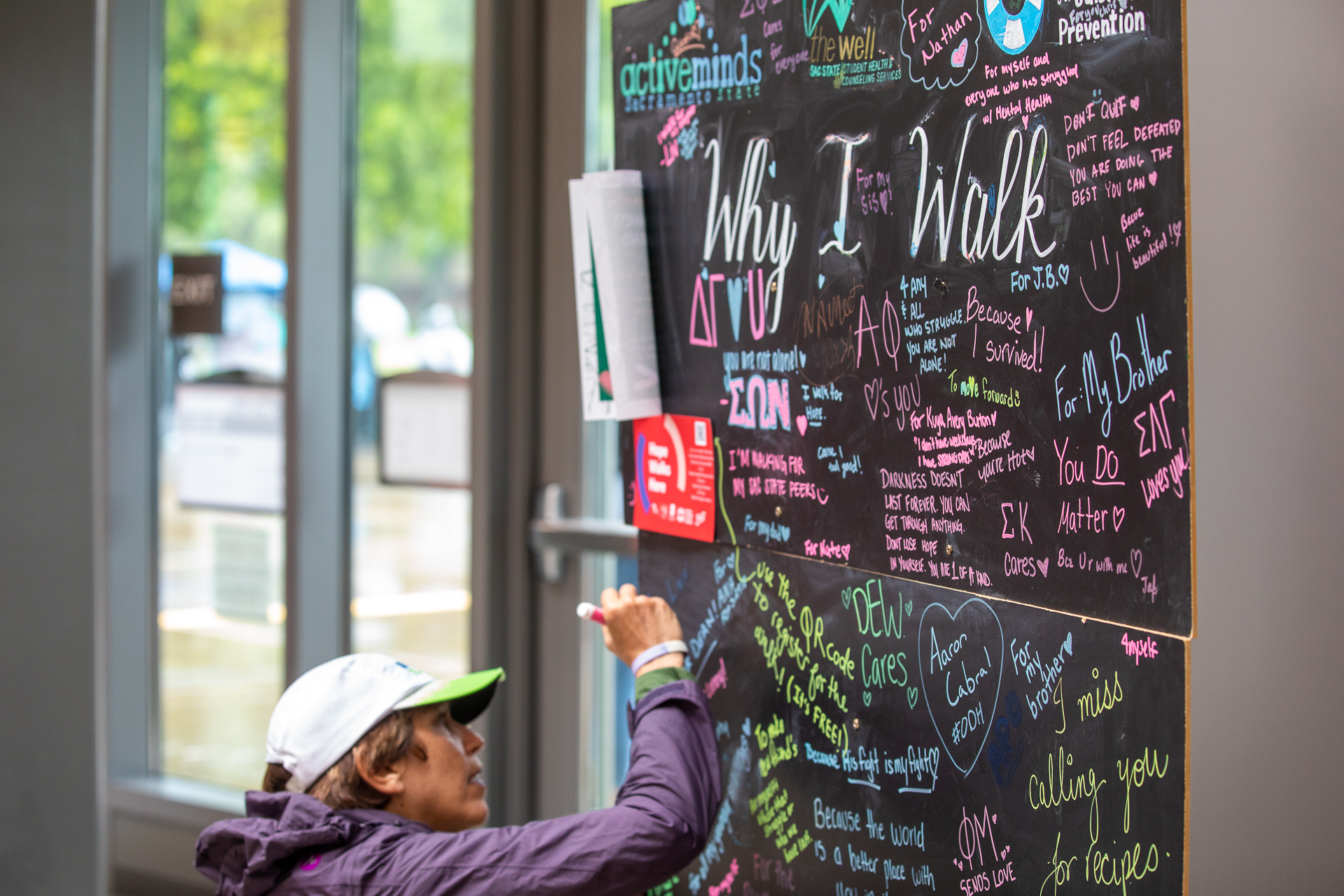 A woman writes on a large, black chalkboard filled with messages about "Why I Walk" from Out of the Darkness participants