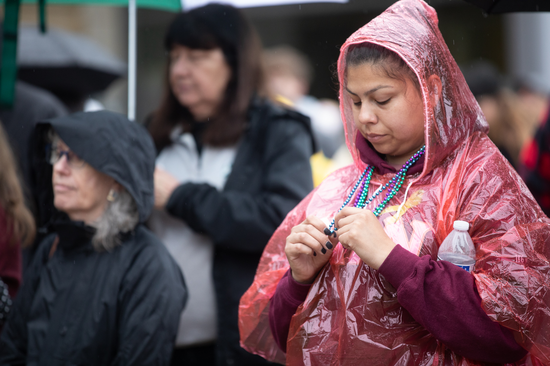 A woman wearing a poncho holds and looks down at necklaces made of blue, green and purple beads