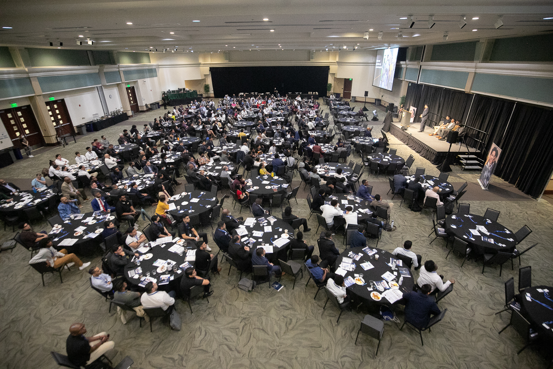 Overhead view of the Young Males of Color conference, with participants at tables and a stage on the right