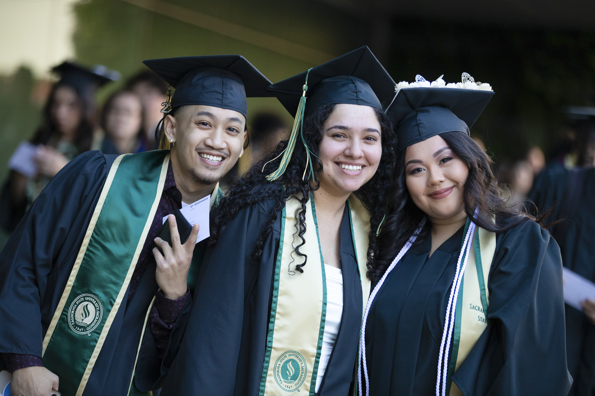 Three graduating students, in academic regalia, indoors, smiling