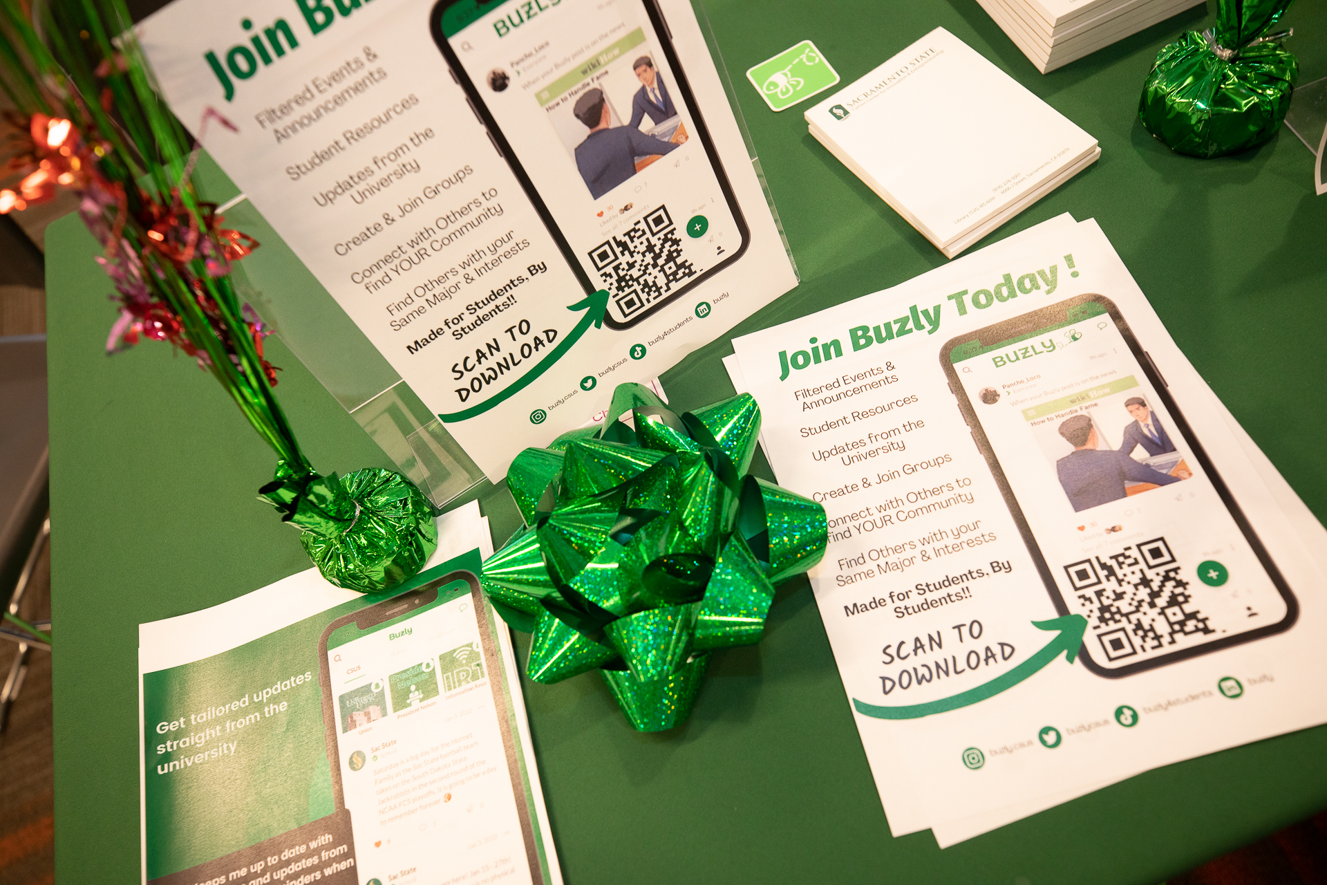 A table with a green tablecloth, with flyers about the Buzly app and decorative items on top