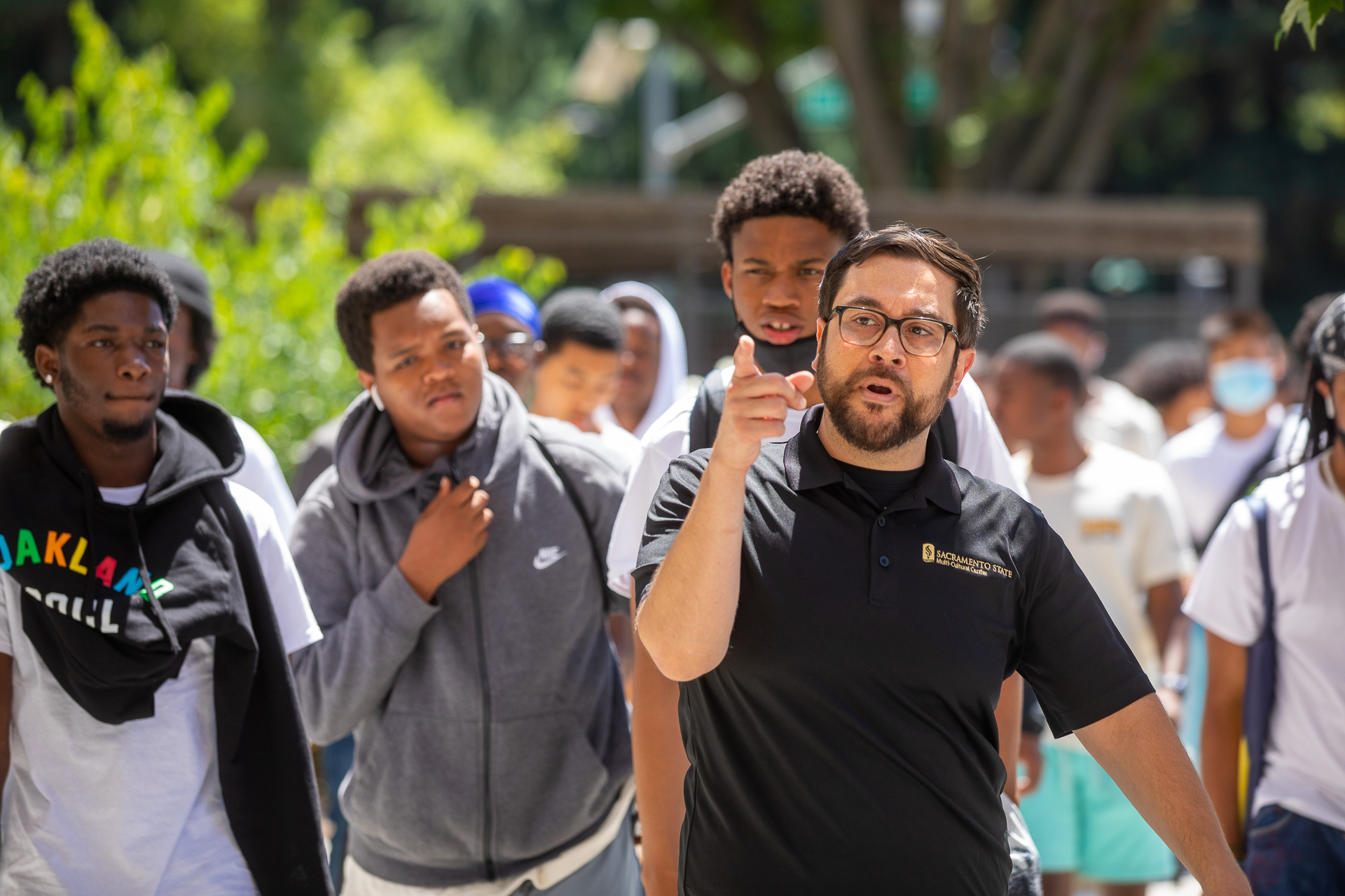 Erik Ramirez, outdoors, pointing as he walks, leading a group of Oakland High School students.