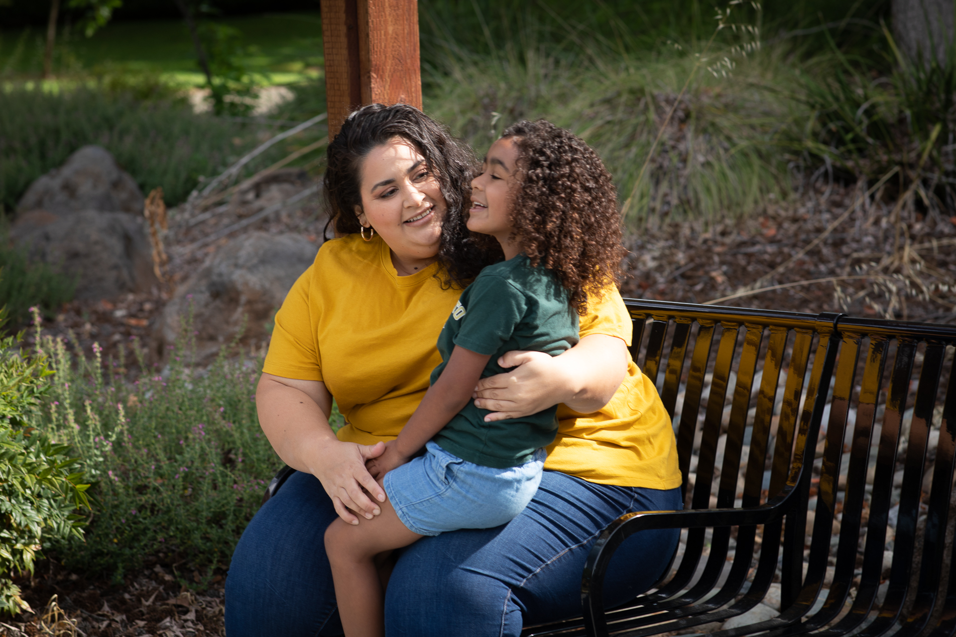Sharon Rodriguez, outdoors on a bench, with her daughter sitting on her lap.