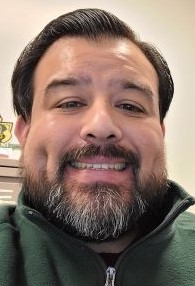 Richard Aguirre, services coordinator of Sac State's Science Educational Equity (SEE) program smiles while wearing a green Sac State Alumni sweatshirt.