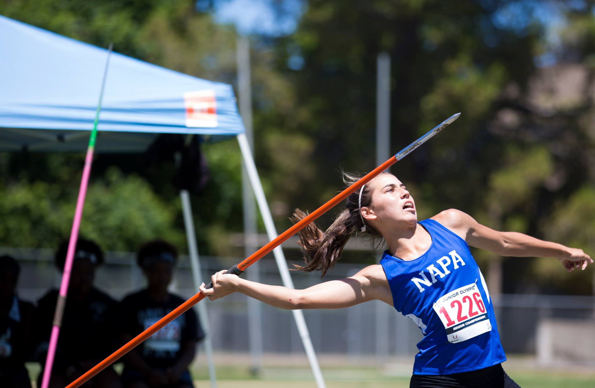 A female competitor with a blue jersey that reads "Napa" prepares to throw a javelin during a USATF National Junior Olympic Track & Field Championships event at Sac State's Hornet Stadium.