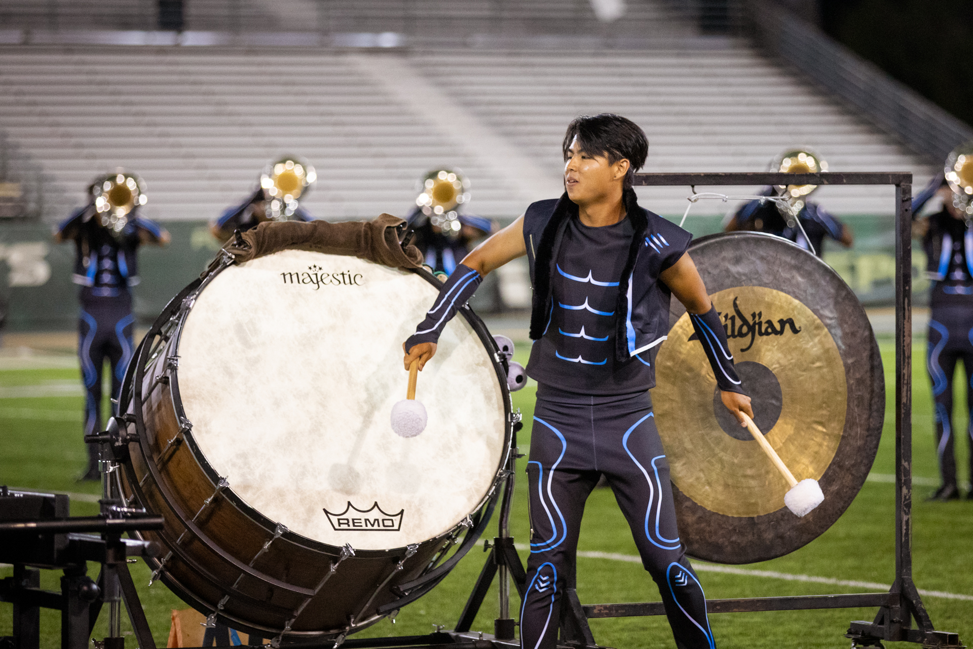 A Sacramento Mandarins drummer dressed in a blue attire performs with a large drum and cymbal on the field at Hornet Stadium.