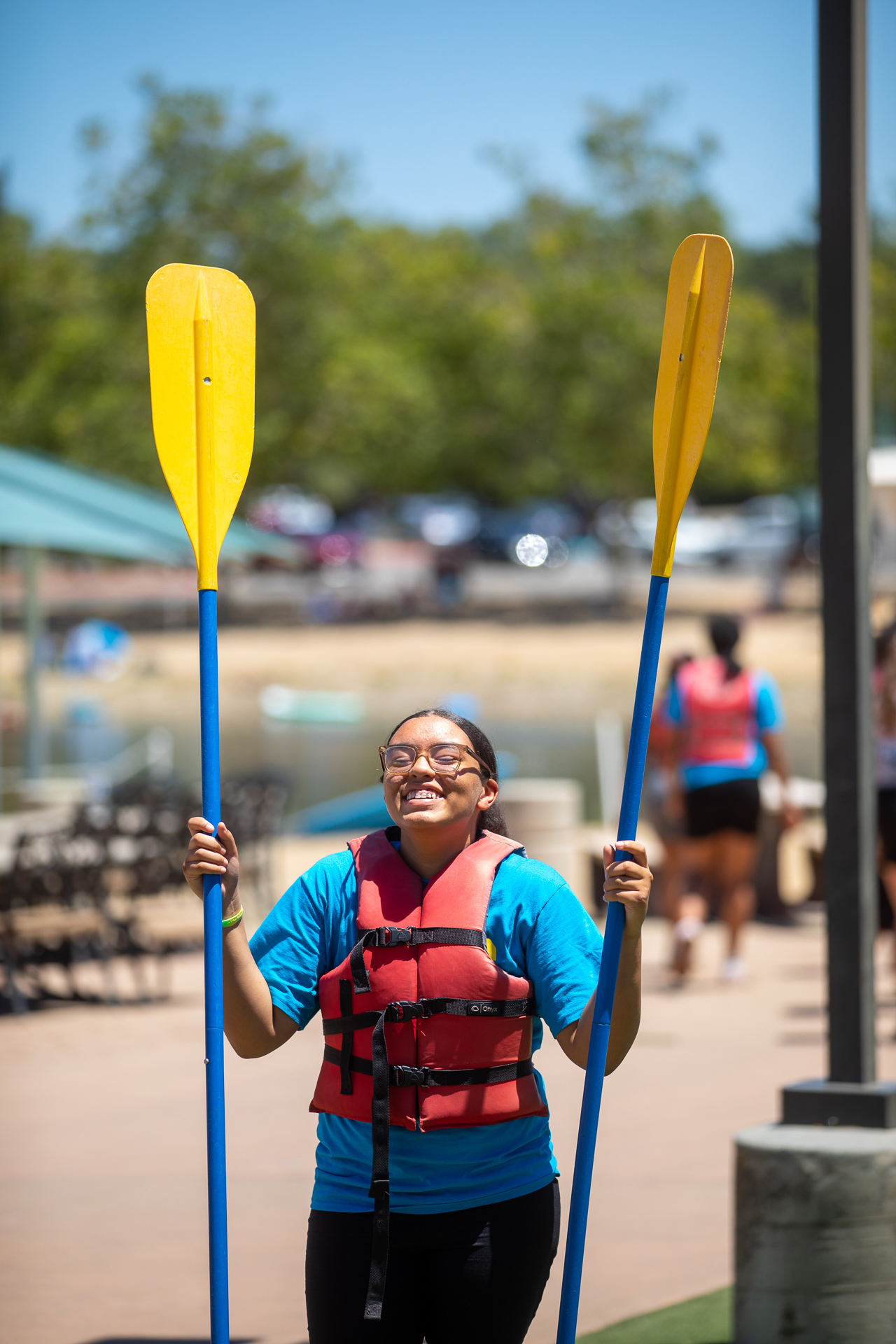 A Roberts Family Development Center Freedom School student smiles and holds two large kayak paddles, one in each arm, at the Sac State Aquatic Center.