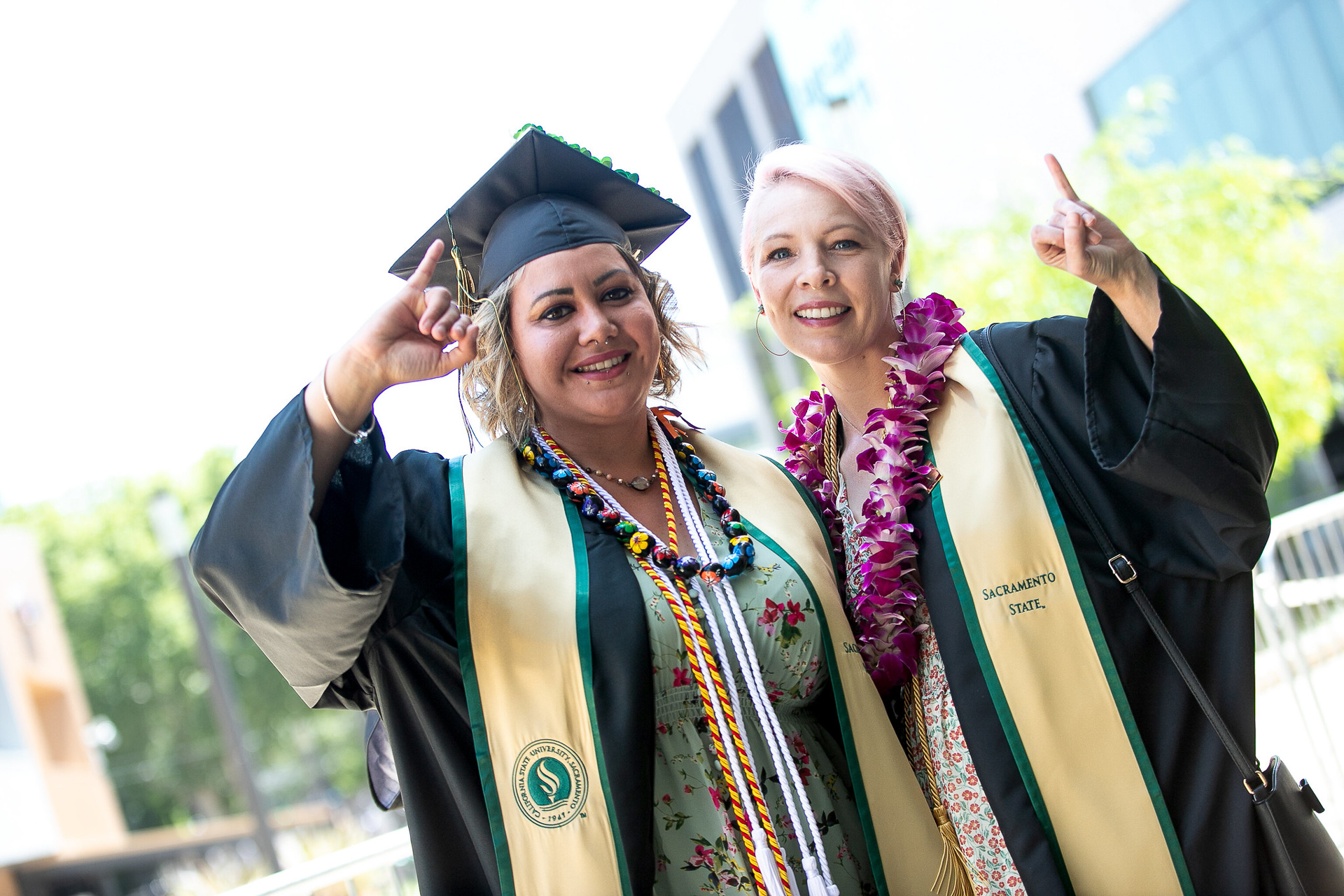 two graduates in regalia show their 'stingers up!'