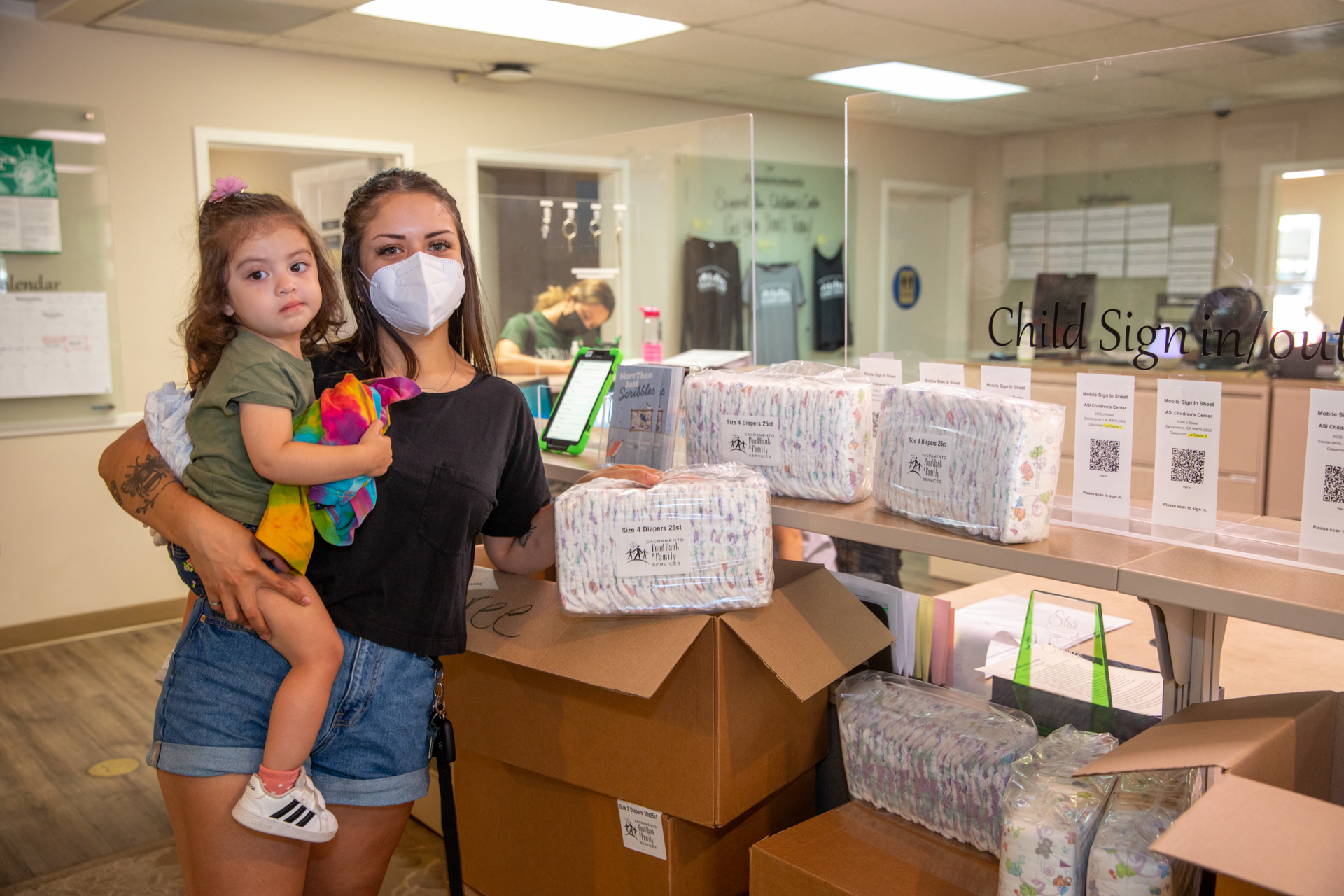 At the ASI Children's Center, working mom and full-time Sacramento State student Gabby McCartney holds a bundle of free-distribution diapers in her left hand while holding her 2-year-old daughter Emilia with her right arm.